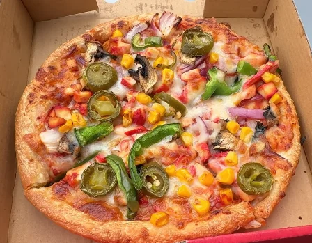 Pizza topped with jalapenos, sweetcorn, green and red peppers and red onion in an open takeaway box